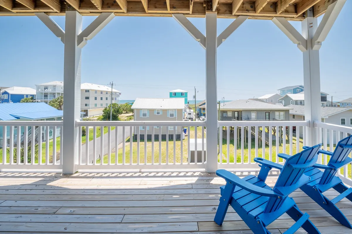 A spacious deck with blue Adirondack chairs overlooking a neighborhood of beach houses and the expansive sky. The open area invites guests to relax, socialize, and drink in the sunrise views directly from the deck.