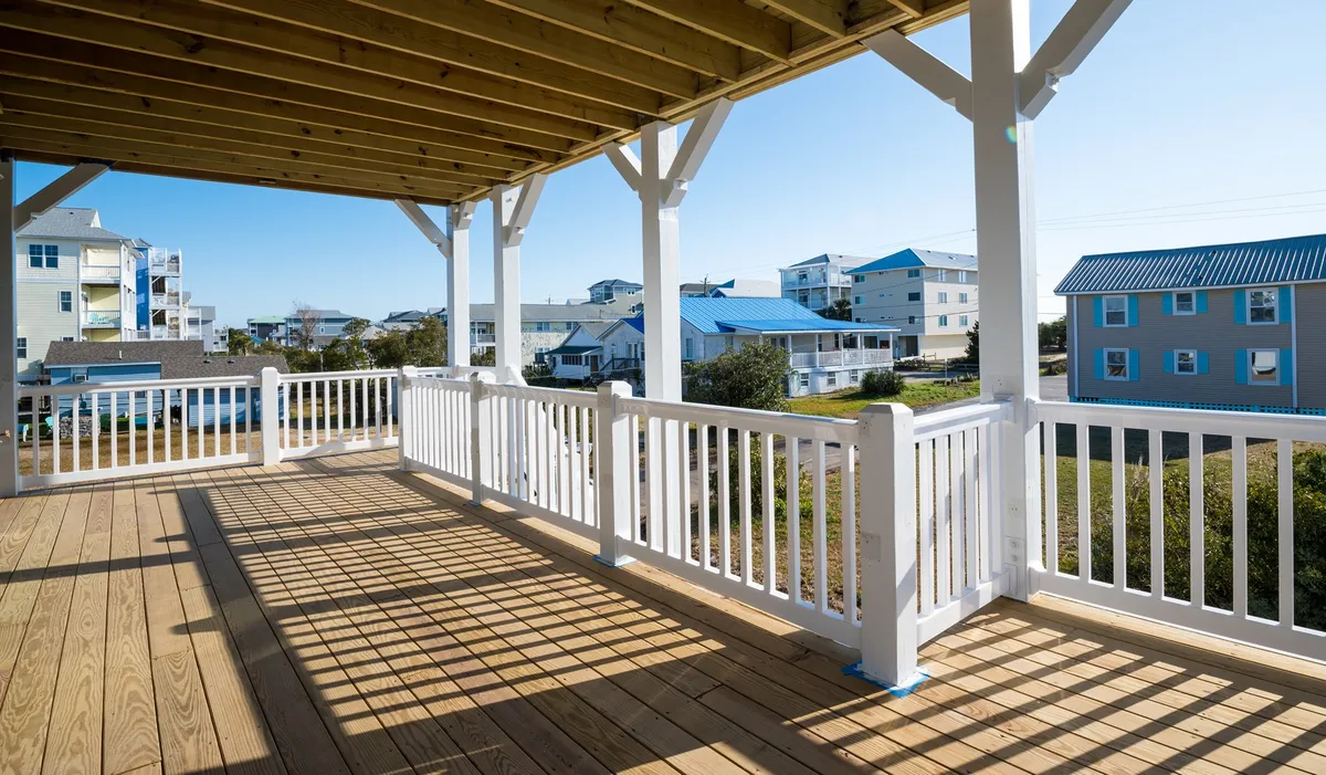 A serene view from a wooden deck with white railings, looking out over blue buildings in the background. The scene evokes a tranquil setting ideal for relaxing with pets after time spent outdoors, and the broad deck offers ample space for dogs and their owners to enjoy the fresh air.