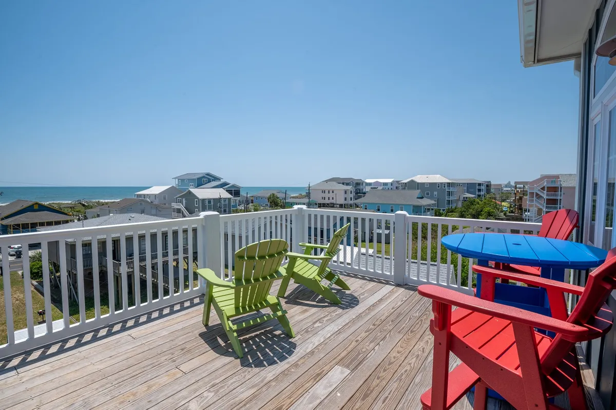 A cheerful exterior deck scene with colorful Adirondack chairs, a wooden deck, and an open view of the ocean. The space invites relaxation and socializing, perfect for enjoying sunrise coffee or sunset cocktails.