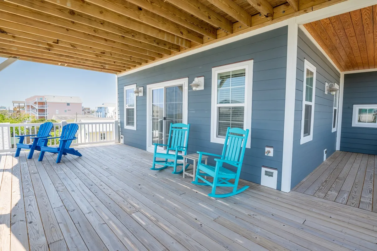 A wooden deck features blue rocking chairs arranged outside a light blue house. The setup suggests a restful spot to enjoy the view, socialize, or prepare for the next outdoor activity.