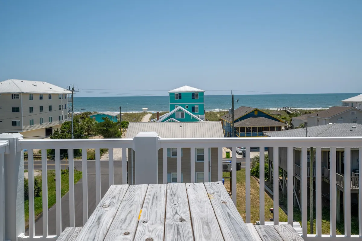 A breathtaking balcony perspective with wooden railings, featuring a sweeping ocean view and colorful beach houses in the distance. The scene radiates tranquility and the lure of sunset or ocean-watching from a private vantage point.