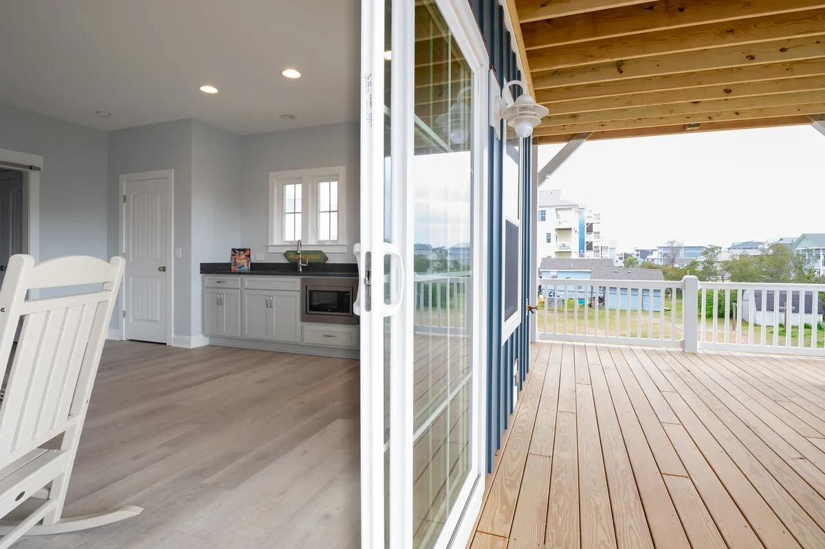 This image captures a cozy, multi-use lounge area with rocking chairs positioned near a kitchenette and a deck with railing in the background. The relaxed setup illustrates a secondary living space, perfect for unwinding, snacking, or socializing.