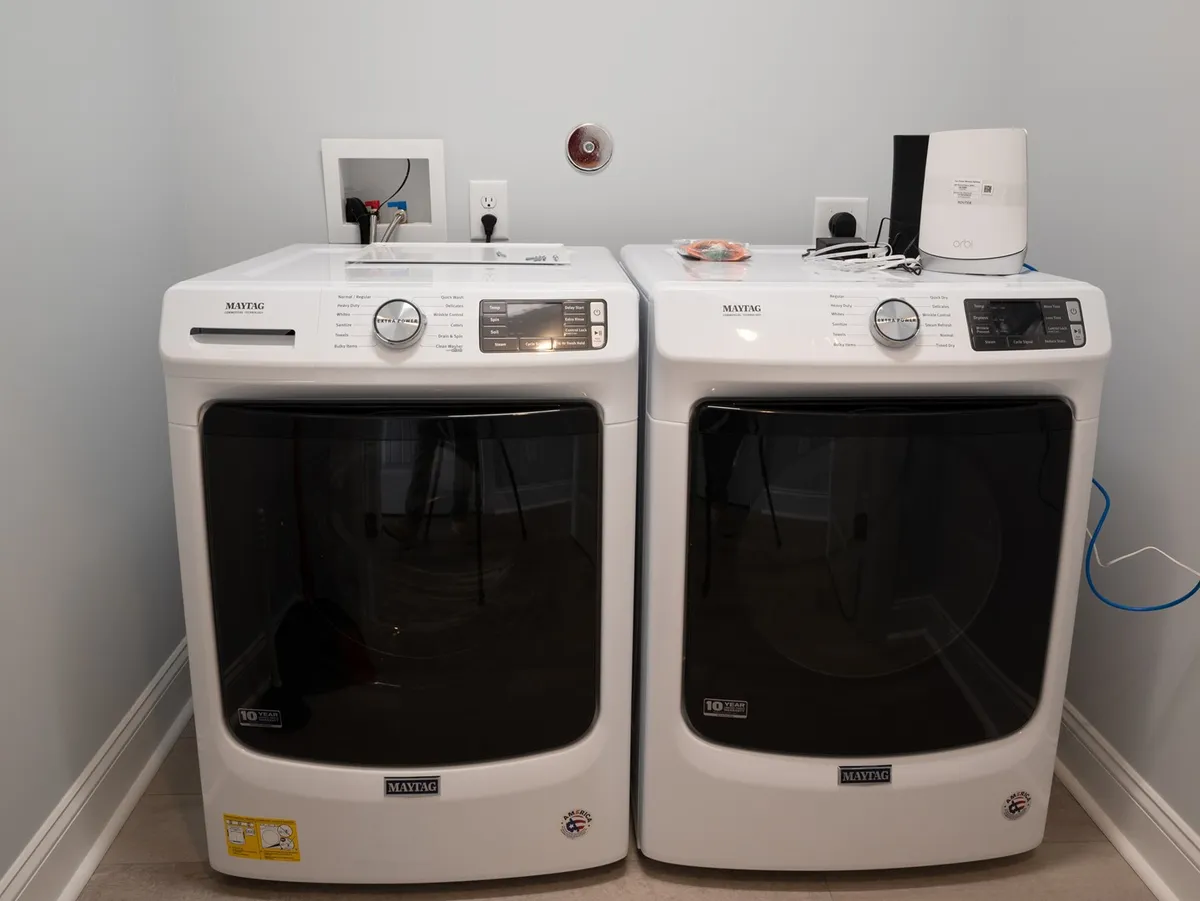 A functional laundry room featuring a washing machine, dryer, and shelves stocked with laundry supplies, presenting a modern, efficient space for handling vacation laundry needs.