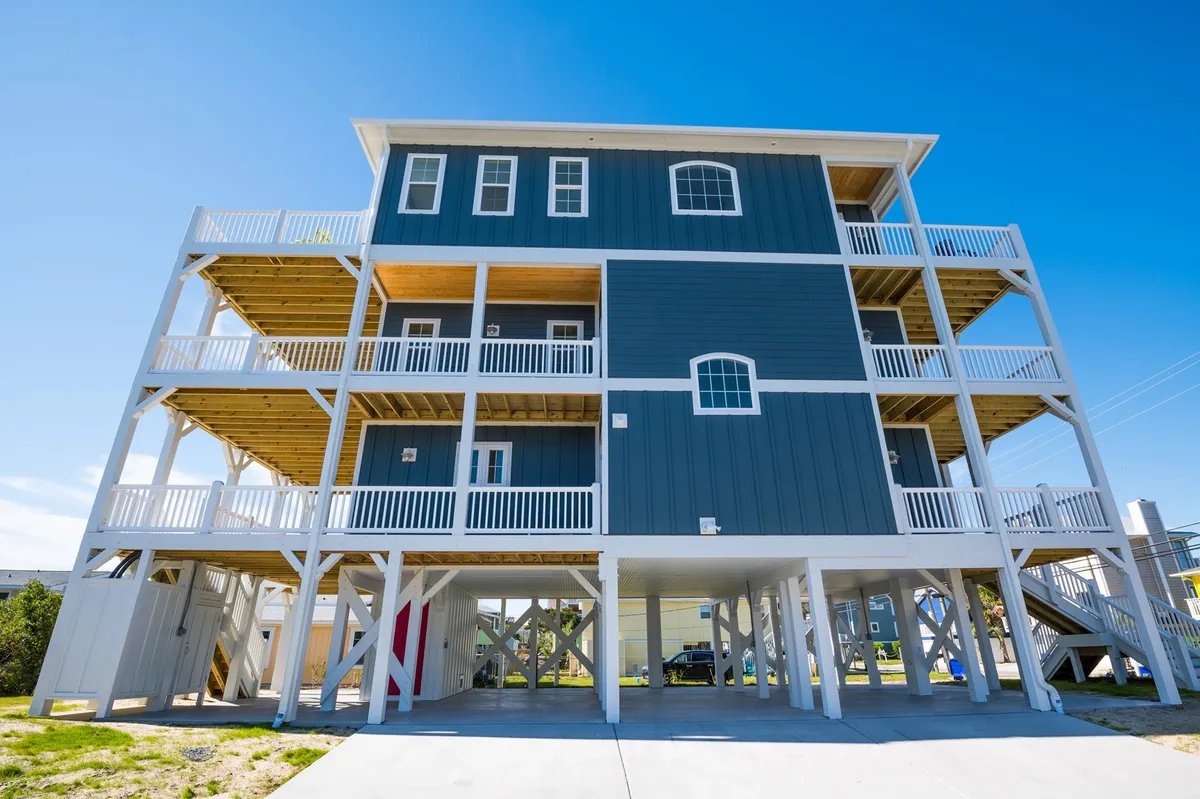 The welcoming exterior of the three-story Patriots Place property, complete with multiple balconies and sturdy support beams. The image conveys ample outdoor living spaces ideal for relaxing, socializing, and making the most of sunset views.