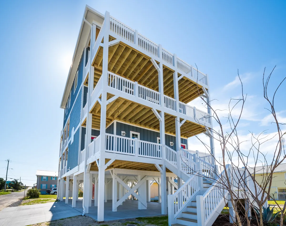 A vibrant exterior shot of Patriots Place, showcasing its multi-level structure with open balconies and sturdy staircases. Several family members and possibly dogs are gathered on the balconies, suggesting a lively, welcoming atmosphere for group gatherings and pet-friendly stays. The image is set during sunset, bathing the scene in warm, cheerful light.